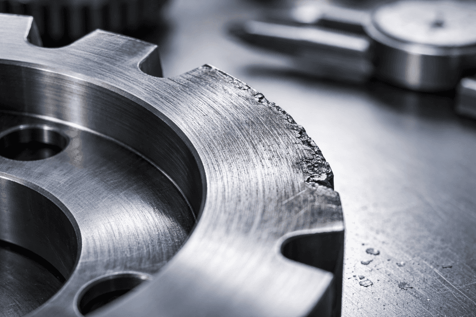 Close-up of an industrial metal edge with visible abrasion wear patterns and textured surface damage.