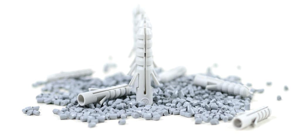 Graues Plastikgranulat auf weißem Hintergrund mit grauen, spritzgegossenen Dübeln